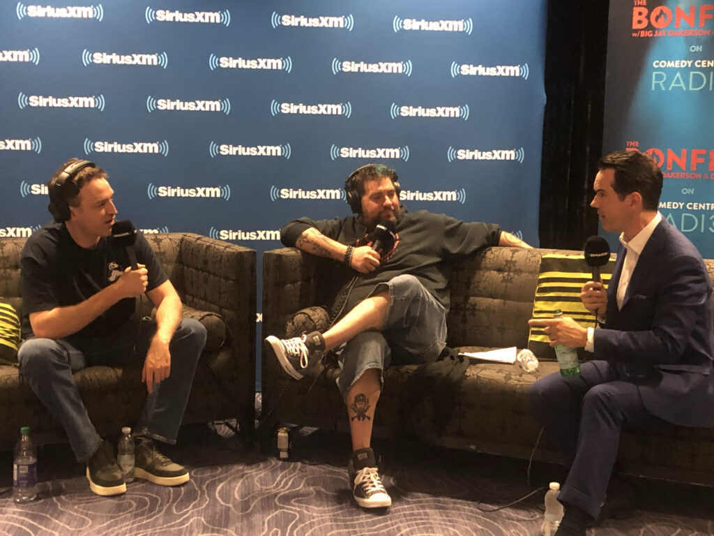 People sit on a couch during an interview against a backdroop with the SiriusXM logo on it.